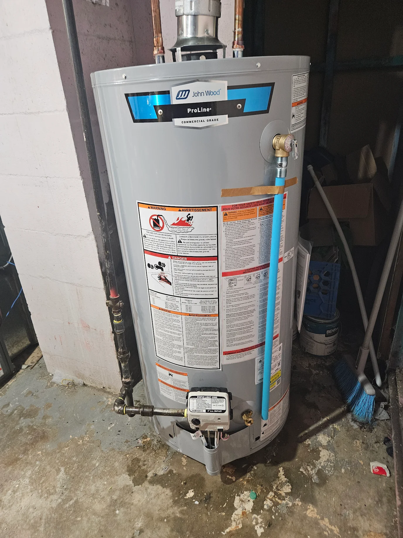 Gray John Wood ProLine commercial water heater with warning labels in a basement corner.