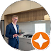 Man in suit standing in a modern kitchen with wooden cabinets and a countertop.