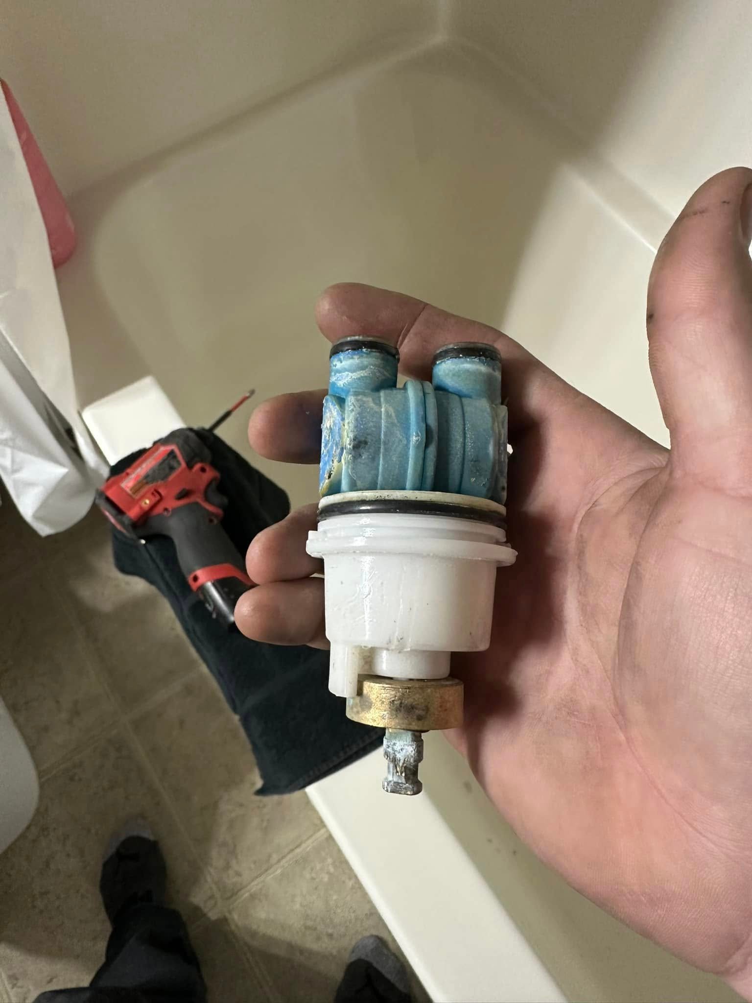 Hand holding a worn blue and white faucet cartridge inside a bathroom with tools in the background.