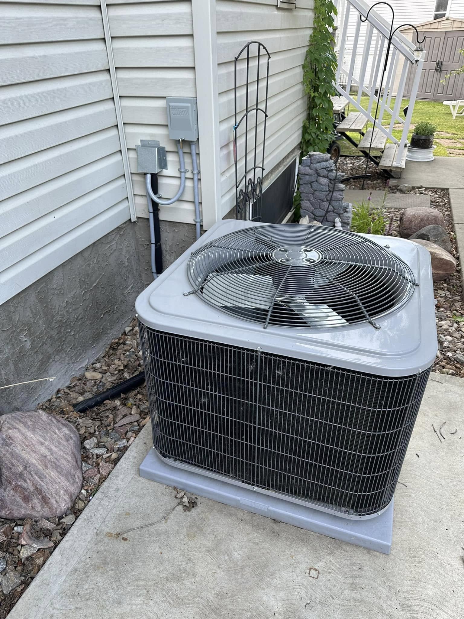 Outdoor air conditioning unit beside a house with vinyl siding and concrete slab base.