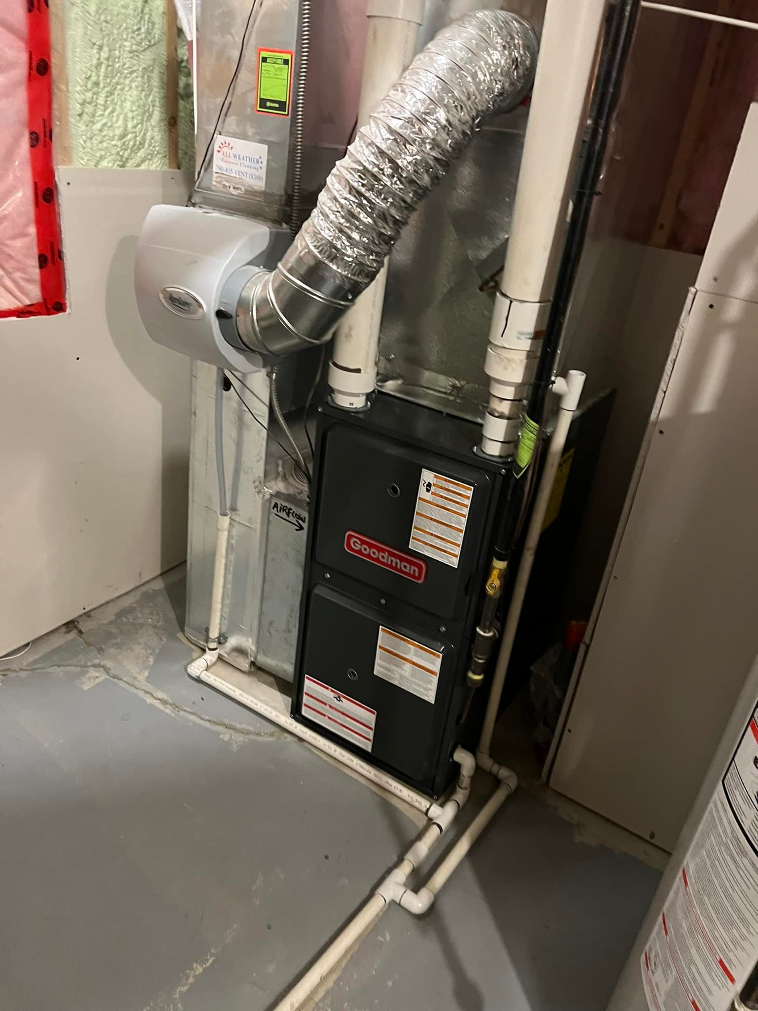 Goodman furnace unit with ductwork and white PVC piping installed on a basement concrete floor.