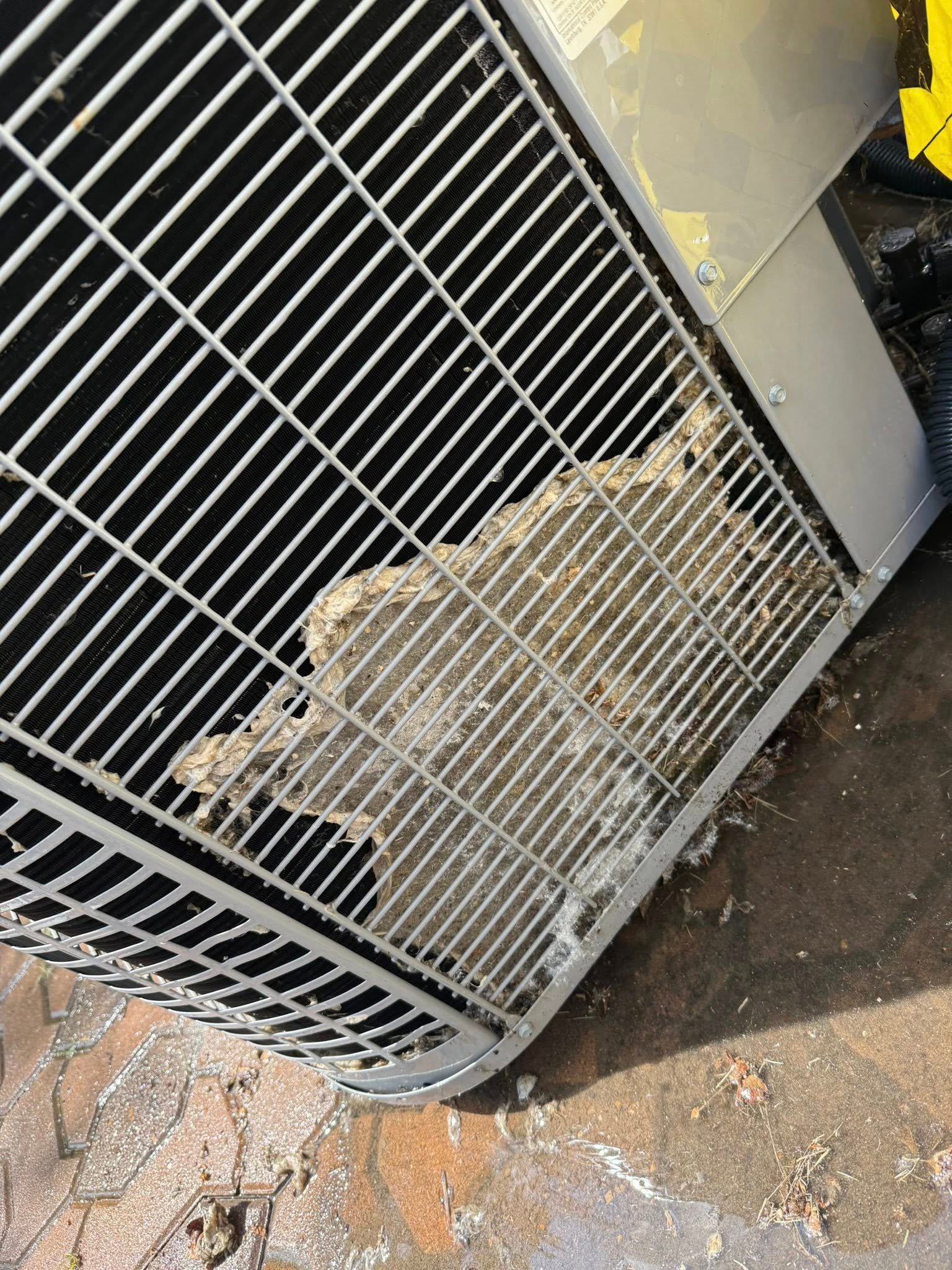 Metal outdoor air conditioning unit with torn insulation visible behind the protective grille.