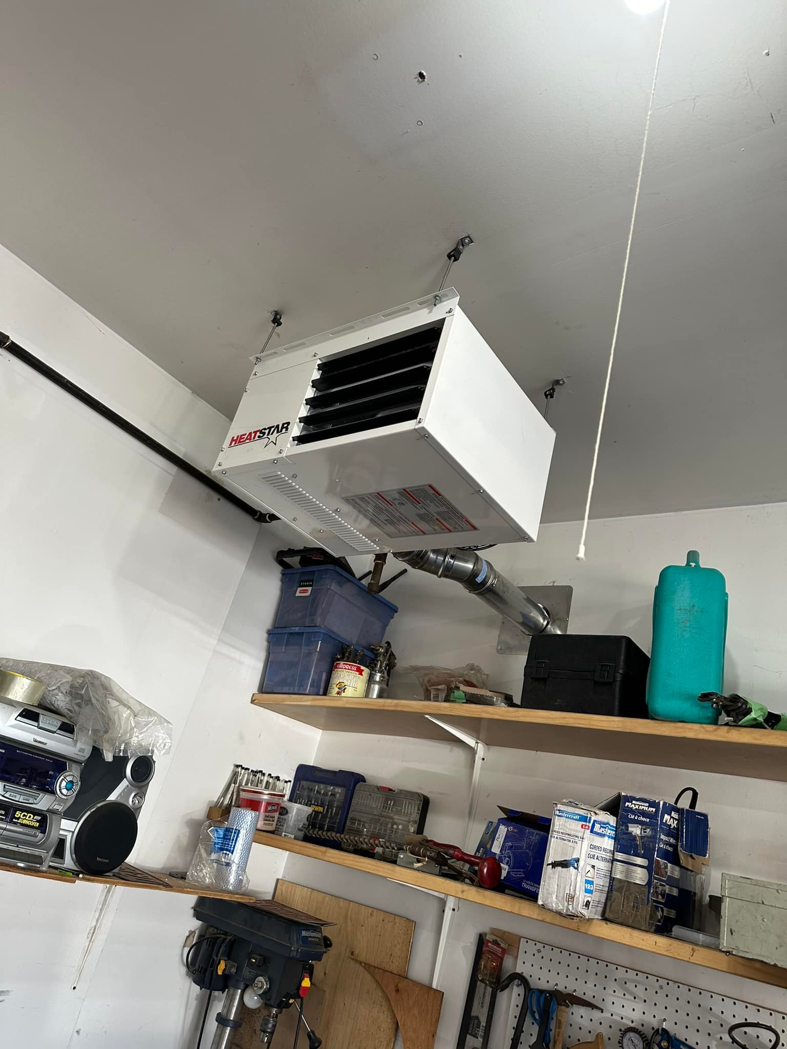 White HeatStar heater mounted on garage ceiling with shelves holding tools and containers below.