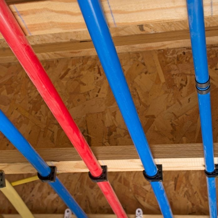 Red and blue plastic pipes mounted on wooden ceiling joists in a construction setting.